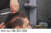 With skilled and precise movements, the experienced barber carefully cuts the ends of the young male client's hair. Стоковое видео, видеограф Strunov David / Фотобанк Лори