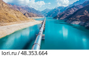 Pipeline traverses reservoir: An engineering marvel spanning turquoise water amid majestic mountain. Стоковое AI-изображение, AI-художник Данила Большаков / Фотобанк Лори