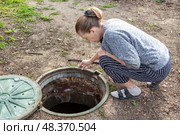 A woman looks into an open septic tank to check the level of sewer discharge. Septic tanks in a country house. Стоковое фото, фотограф Коханова Наталья / Фотобанк Лори