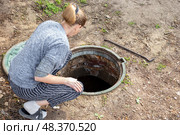 A woman looks into an open septic tank to check the level of sewer discharge. Septic tanks in a country house. Стоковое фото, фотограф Коханова Наталья / Фотобанк Лори