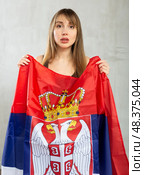 Sad young woman holding flag of Serbia against unicoloured background. Стоковое фото, фотограф Яков Филимонов / Фотобанк Лори
