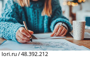 A person in a chunky blue sweater is deeply focused on a brainstorming session, jotting down ideas while enjoying a warm beverage in a cozy indoor atmosphere decorated with soft lighting. Стоковое AI-видео, аниматор Данила Большаков / Фотобанк Лори