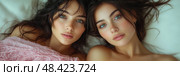 Two young women with captivating blue eyes lay side by side on a bed, exuding a sense of tranquility and intimacy in a cozy indoor setting. Стоковое AI-изображение, AI-художник Данила Большаков / Фотобанк Лори