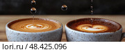 Richly brewed coffee in two cups showcases stunning latte art, enhanced by droplets falling, creating an inviting ambiance in a café. Стоковое AI-изображение, AI-художник Данила Большаков / Фотобанк Лори