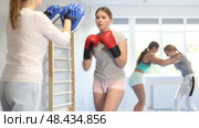 Focused teenage girl wearing boxing gloves working out with female coach during self-defense course, practicing punches on mitts. Стоковое видео, видеограф Яков Филимонов / Фотобанк Лори