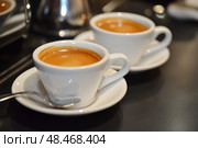 Two Espresso cups with coffee. Freshly brewed espresso shots on a dark wooden table with copy space, background, caffeine. Espresso cups, spoons, saucers. Refreshing hot cup of strong coffee at a cafe. Стоковое AI-изображение, AI-художник Марина Демидюк / Фотобанк Лори