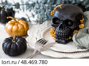 A mysterious black skull with golden roses and pumpkins on serving plates for a Halloween or Day of the Dead party. Стоковое фото, фотограф Photojuli / Фотобанк Лори