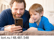 Father and son little boy laughing and using phone. They watching funny videos together, playing games on smartphone. Concept technology, smart phone addicted. Fun weekend activity. Modern fatherhood. Стоковое фото, фотограф Марина Демидюк / Фотобанк Лори