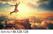 A man leaps off a rocky cliff, soaring through the clear blue sky with arms outstretched in a thrilling freefall. Стоковое AI-изображение, AI-художник Данила Большаков / Фотобанк Лори