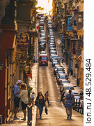 VALLETTA, MALTA - NOVEMBER 12, 2018 - Hilly ancient streets view with colourful balconies, people and cars in the medieval city. Редакционное фото, фотограф Сергей Богомяко / Фотобанк Лори