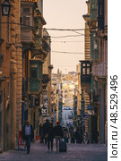VALLETTA, MALTA - NOVEMBER 12, 2018 - Hilly ancient streets view with colourful balconies, people and cars in the medieval city. Редакционное фото, фотограф Сергей Богомяко / Фотобанк Лори