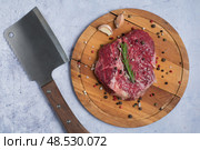 Сырой стейк Рибай со специями и веточкой розмарина на круглой деревянной доске с резаком на мраморном фоне. Вид сверху. Стоковое фото, фотограф Максим Коломыченко / Фотобанк Лори