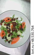 Professional chef wearing black gloves sprinkling crispy croutons over gourmet salmon salad with fresh arugula, creating elegant final garnish on white plate. Стоковое видео, видеограф Данил Руденко / Фотобанк Лори
