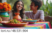 Close up of festive table, featuring a colorful tablecloth, traditional pottery, and centerpiece of marigold flowers. Happy couple sitting on it. Cinco de Mayo. Independence Day. Fiesta and festival. Стоковое AI-видео, аниматор Sergey Grishin / Фотобанк Лори