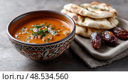 Moroccan Harira Soup in a Bowl with Flatbread and Dates, rich earthy tones. Марокканский суп харира в миске с лепешками и финиками. Стоковое AI-изображение, AI-художник Katsiaryna Repich / Фотобанк Лори