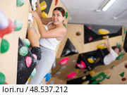 Young Europian woman climbs steep artificial wall in sports complex and trains endurance. Стоковое фото, фотограф Яков Филимонов / Фотобанк Лори