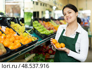 Asian female seller in apron chooses ripe mandarin. Стоковое фото, фотограф Яков Филимонов / Фотобанк Лори