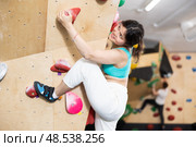 Young Asian woman climbs steep artificial wall in sports complex and trains endurance. Стоковое фото, фотограф Яков Филимонов / Фотобанк Лори