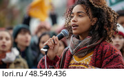 A woman stands in front of a large crowd, holding a microphone and speaking. The audience attentively listens to her speech. Стоковое AI-изображение, AI-художник Данила Большаков / Фотобанк Лори