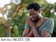 Sad African American male with a pained expression holds his shoulder, suggesting discomfort or injury, set against an outdoor backdrop with soft lighting. Стоковое AI-изображение, AI-художник Данила Большаков / Фотобанк Лори