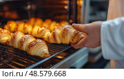 Freshly baked croissants being taken out of oven by baker, showcasing golden flaky texture, warmth, and the artisanal quality of classic pastry making. Стоковое AI-изображение, AI-художник Катерина Бондарец / Фотобанк Лори