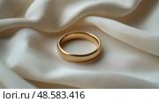 Gold wedding ring resting on elegant satin fabric at a romantic setting. Золотое обручальное кольцо на элегантной атласной ткани в романтической обстановке. Стоковое AI-изображение, AI-художник Katsiaryna Repich / Фотобанк Лори