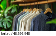 Stylish linen shirts and cotton trousers showcased on hangers in a vibrant. Стильные льняные рубашки и хлопковые брюки, вывешенные на вешалках в ярких. Стоковое AI-изображение, AI-художник Katsiaryna Repich / Фотобанк Лори
