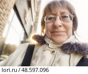 Middle-aged woman enjoying a sunny day while documenting her travel adventures in a cozy neighborhood. Стоковое фото, фотограф Кривошеина Елена Леонидовна / Фотобанк Лори