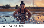 A young woman wearing a sports bra lowers her body into a puddle of water, splashing it around her. Стоковое AI-изображение, AI-художник Данила Большаков / Фотобанк Лори