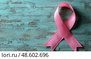 A pink ribbon rests on a textured blue surface, representing solidarity and support for breast cancer awareness initiatives and survivors. Стоковое AI-изображение, AI-художник Данила Большаков / Фотобанк Лори