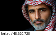 A man wearing a red and white keffiyeh gazes thoughtfully, showcasing his rugged features and deep contemplation in low light. Стоковое AI-изображение, AI-художник Данила Большаков / Фотобанк Лори