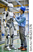 Man Inspecting HZ Standard Scale X Next to Robot in Factory. Generative AI. Стоковое AI-изображение, AI-художник Roman Zavorotny / Фотобанк Лори