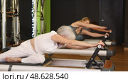 Mature woman sitting on foldable bed reformer performs exercises, strengthening body and muscles. Стоковое видео, видеограф Яков Филимонов / Фотобанк Лори
