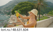 Woman admiring lemon with townscape Amalfi and hills in background, celebrating golden citrus fruit beneath coastal skies and timeless cliffs. Стоковое видео, видеограф Igor Tichonow / Фотобанк Лори