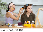 Woman curling hair with rollers to female friend at home. Стоковое фото, фотограф Яков Филимонов / Фотобанк Лори