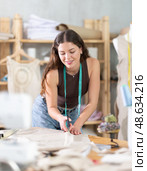 Young female dressmaker cutting textile in sewing workshop. Стоковое фото, фотограф Яков Филимонов / Фотобанк Лори