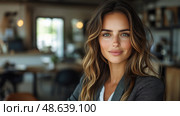 A smiling woman with wavy hair and hazel eyes stands confidently in a modern café filled with natural light, exuding positivity and approachability. Стоковое AI-изображение, AI-художник Данила Большаков / Фотобанк Лори