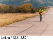 Triathlete riding his bicycle during sunset, preparing for a marathon. The warm colors of the sky provide a beautiful backdrop for his determined and focused effort. Стоковое фото, фотограф Benis Arapovic / PantherMedia / Фотобанк Лори