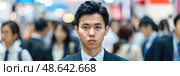 A young man in formal attire stands out with a serious expression while crowds of professionals move around him at a bustling event downtown. Стоковое AI-изображение, AI-художник Данила Большаков / Фотобанк Лори