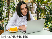 Young woman works with laptop on terrace of  cafe. Hunched posture, professional spinal deformity concept. Стоковое фото, фотограф Алена Аксенова / Фотобанк Лори