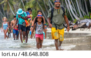 Families and friends wade through shallow water at a tropical beach, smiling and enjoying time together under the sun. Стоковое AI-изображение, AI-художник Данила Большаков / Фотобанк Лори