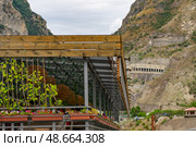 A contemporary building showcases greenery and floral arrangements beneath a wooden roof, set against a dramatic mountainous backdrop, Главрыба, Республика Дагестан, Казбековский район, село Ново-Зубутли. Стоковое фото, фотограф Данила Большаков / Фотобанк Лори
