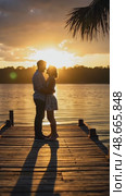 A couple sharing a quiet moment at sunset by the lake, golden light reflecting on the water, their silhouettes creating long shadows. Стоковое AI-видео, аниматор Sergey Grishin / Фотобанк Лори