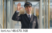 Smiling airline pilot waving hand in airport terminal. Стоковое AI-видео, аниматор Юрий Поздников / Фотобанк Лори