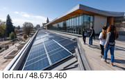 Solar panels on the roof of an energy-efficient school building, surrounded by students. Aerial view of the solar panels on the roof. modern buildings with classrooms and student residences. Стоковое AI-изображение, AI-художник ALLA YURTAYEVA / Фотобанк Лори