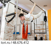 Man visitor performs exercises in hanging position on combined Pilates trapeze table. Стоковое фото, фотограф Яков Филимонов / Фотобанк Лори