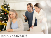 Woman and man swear at old mother who puts up with it at сhristmas while sitting at kitchen tabl. Стоковое фото, фотограф Яков Филимонов / Фотобанк Лори