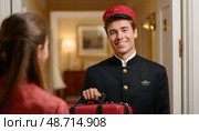 Bellboy carrying luggage smiling at hotel guest. Стоковое AI-изображение, AI-художник Юрий Поздников / Фотобанк Лори