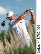 A man is swinging a golf club in a field of tall grass. Стоковое AI-изображение, AI-художник Ярославский Максим / Фотобанк Лори