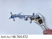 Detaching outdated plumbing fixture to install modern faucet, worker carefully loosens connections on wall-mounted tap above sink. Стоковое фото, фотограф Владимир Григорьев / Фотобанк Лори